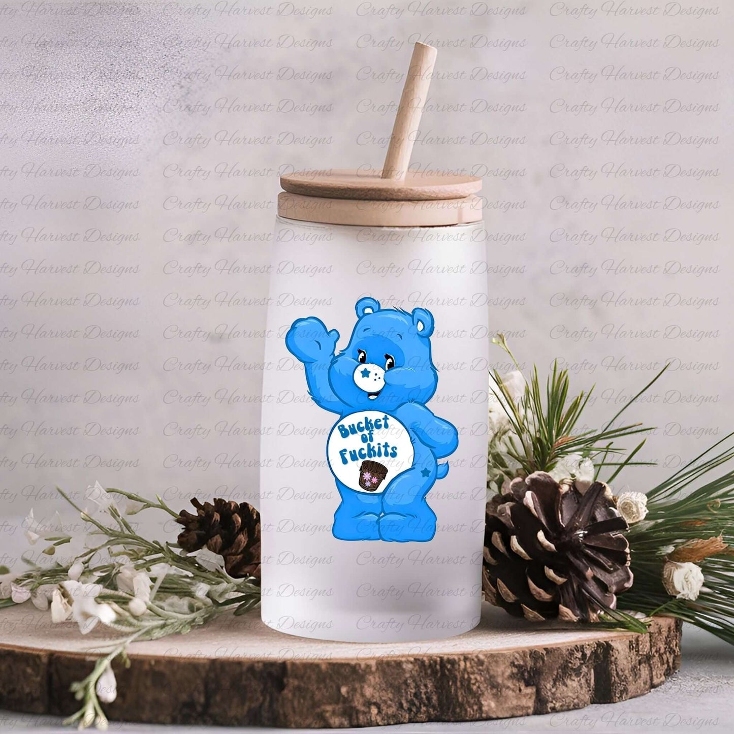 Frosted glass jar-style tumbler with a wooden lid and straw, featuring the blue Swear Bear with the phrase “Bucket of Fuckits” on the belly. The tumbler is displayed with pinecones and greenery decor.