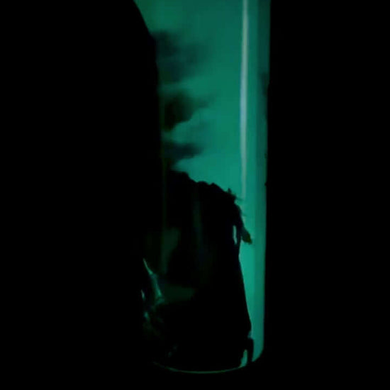 Glow-in-the-dark 20oz tumbler featuring a Grim Reaper design, illuminated in green light in a dark setting, showcasing the full wrap effect.